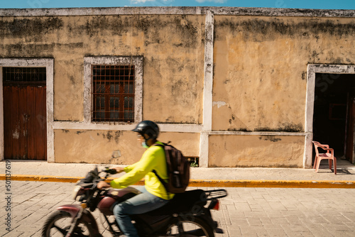 beautiful building beige wall moldy texture shaby. two arched entrances with doors. motobike passing by. streets of a mexican city valladolid