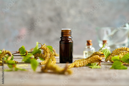 Fotografia A dark bottle of essential oil with birch branches with catkins in spring