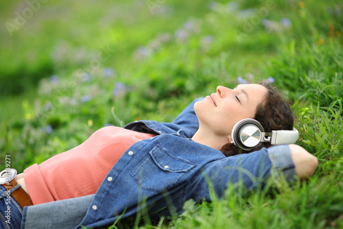 Relaxed woman lying on the grass listening to music photo