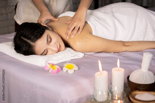 Healthy Asian Thailand woman lying in bed doing spa treatment on her back. was compressed with herbs wrapped in a white cloth massage her back to relax There were flowers and candles on the bed.