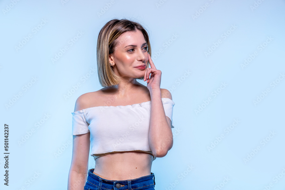 Young caucasian girl with light blue eyes smiles looking outside the frame - Studio photography of pretty happy woman thinking about an idea smiling Young caucasian girl with light blue eyes smiles looking outside the frame - Studio photography of pretty happy woman thinking about an idea smiling