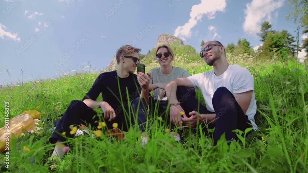 Three friends are sitting on a slope and looking at photos on their phone in a mountainous area. Tourism and travel Three friends are sitting on a slope and looking at photos on their phone in a mountainous area. Tourism and travel
