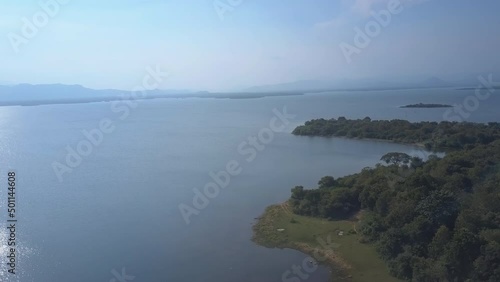 Wallpaper Mural Green trees grow in tropical forest surrounded by blue water lake against distant mountains. Udawalawe National Park Safari aerial view Torontodigital.ca