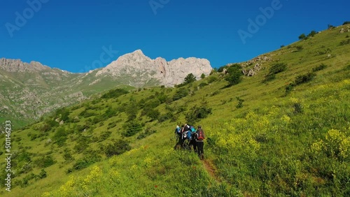 A group of hikers go to the top of mountain. Tourists  hiking on trekking trail to reach mountain's  peak. Khustup mountain in  Armenia, Caucasus. Adventure travel. Rocks and green landscape. photo