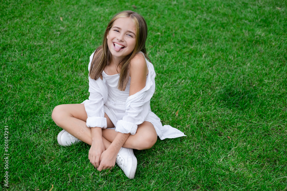 pretty tween girl in white clothes sitting on green grass outside in park on sunny summer day. charming ukrainian child portrait pretty tween girl in white clothes sitting on green grass outside in park on sunny summer day. charming ukrainian child portrait