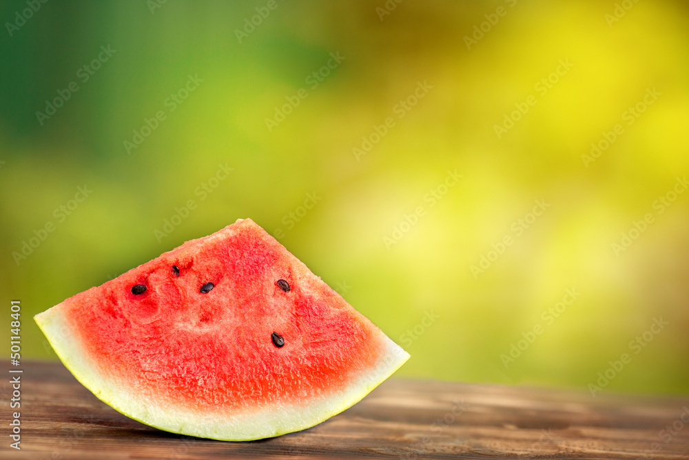 PIECE OF WATERMELON IN THE RAYS OF THE BRIGHT SUMMER SUN IS SITTING ON A WOODEN BOARD PIECE OF WATERMELON IN THE RAYS OF THE BRIGHT SUMMER SUN IS SITTING ON A WOODEN BOARD