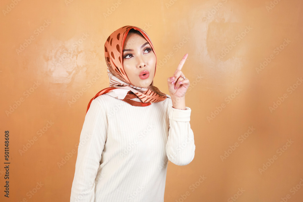 Fototapeta premium Cheerful young Muslim Asian woman pointing above to copy space with smile