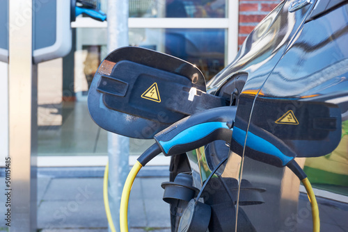 Electric car with blue connector and yellow cable charging at a charging point. Green energy, zero emission or sustainability concept. 