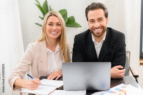 Beautiful and clever young man and woman wearing stylish suits using laptop in cozy office. Working concept. Stock photo