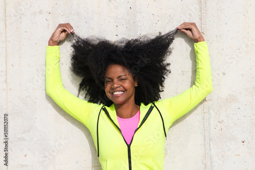 Beautiful young Afro-American woman in bright green and pink sportswear on a grey concrete wall texture background. Woman makes different expressions. Laughing, serious, happy, sad, thinking, hair.