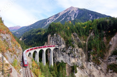 A local train coming out of the tunnel in a vertical cliff  crossing the famous Landwasser Viaduct over a deep gorge with fall colors on the rocky mountainside in Filisur, Grisons, Switzerland photo