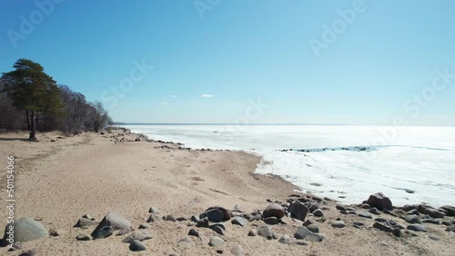 flying over frozen sea bay bay on a sunny day blue sky coastline and rocks. High quality 4k footage