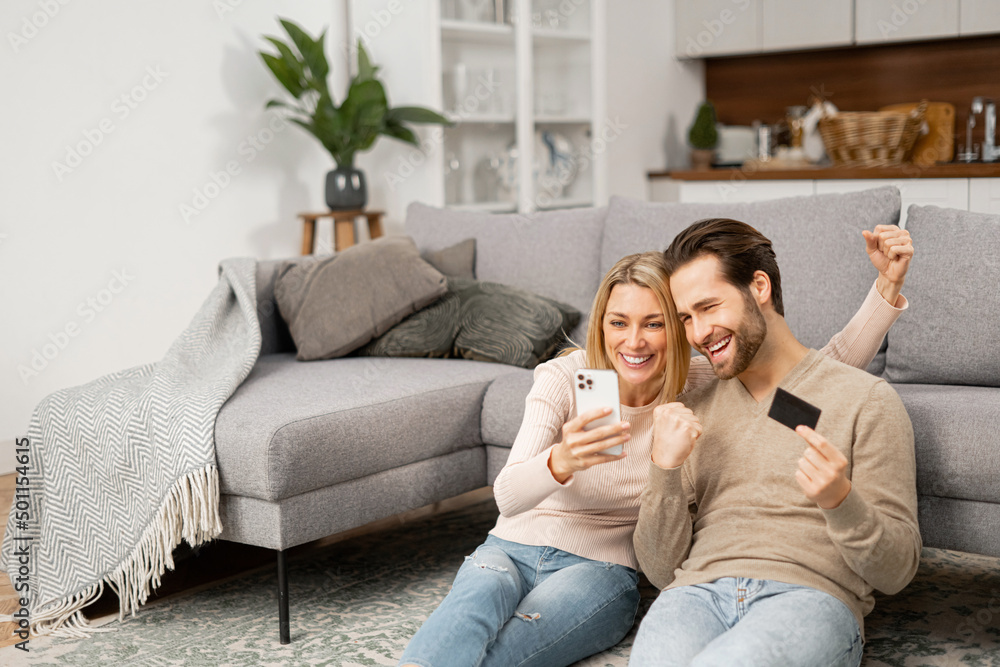 Overjoyed caucasian couple shopping together online. Excited woman and man holding smartphone and credit card, making purchases online, order, buying something in e-shop