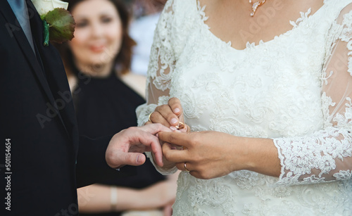 A couple getting married at a wedding ceremony - the bride placing a gold ring on the groom's finger