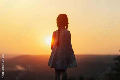 Girl child standing on the hill and watching the sunset.