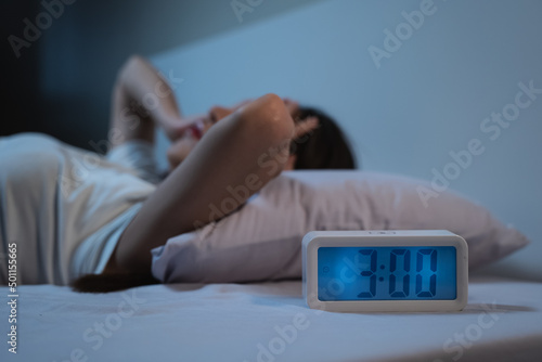 woman have insomnia on the bed selective focus on alarm clock at three in the morning. photo