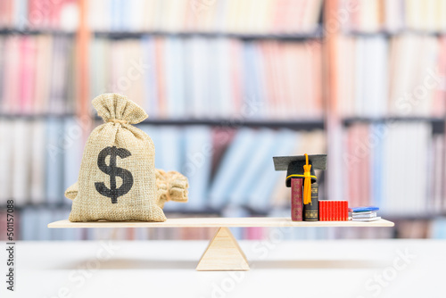Принти на полотні Saving money for college tuition fees, education concept : US dollar bags, a black graduation cap, a mortarboard or a hat, books on a balance scale