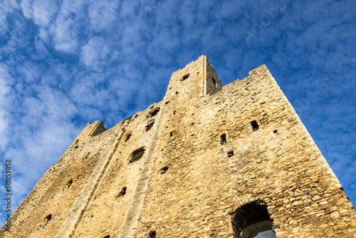 The tower of Rochester Castle, looking up towards the blue sky, with very light clouds.  The sun is shining on the walls.  October 2021.