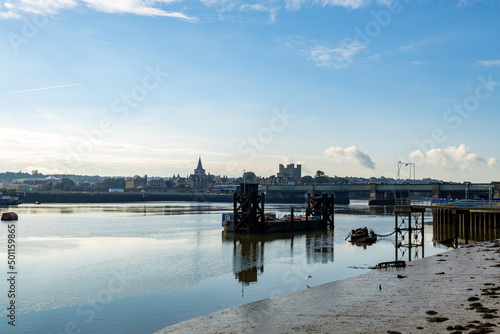 Rochester Castle and Cathedral, from East of the Rochester Bridge, across the Medway River.  A clear autumn day in October 2021. A derelict jetty and dockside equipment are in the river. 