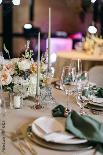 Banquet table is decorated with plates, cutlery, glasses, candles and flower arrangements. Wedding decor