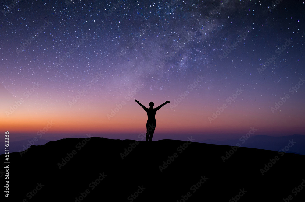 Silhouette of young woman traveler and backpacker watched the star and milky way alone on top of the mountain. She open arms and enjoyed traveling and was successful when he reached the summit.
