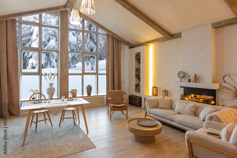 Fototapeta premium cozy warm home interior of a chic country chalet with a huge panoramic window overlooking the winter forest. open plan, wood decoration, warm colors and a family hearth