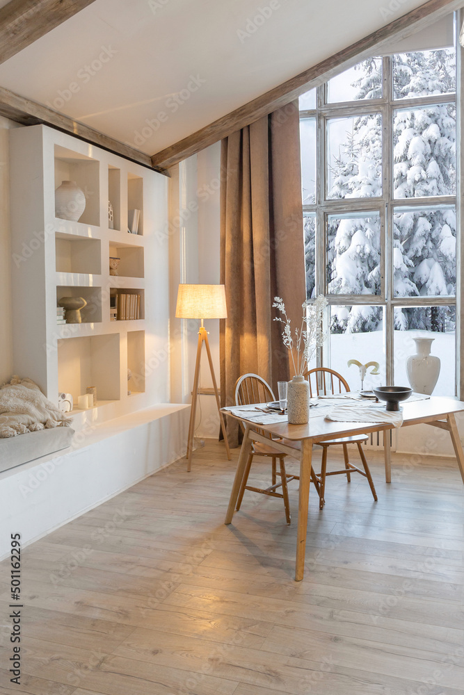 Fototapeta premium cozy warm home interior of a chic country chalet with a huge panoramic window overlooking the winter forest. open plan, wood decoration, warm colors and a family hearth
