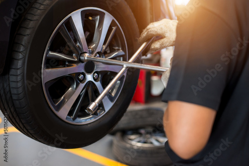 Auto mechanic with electric screwdriver changing tire outside at car service center. Hands replace tires on wheels. Tire installation concept.