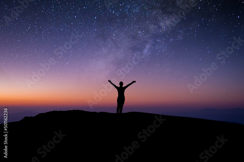 Silhouette of young woman traveler and backpacker watched the star and milky way alone on top of the mountain. She open arms and enjoyed traveling and was successful when he reached the summit.