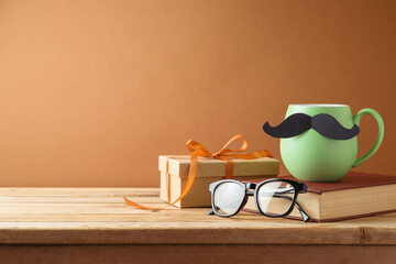 Happy Fathers day concept with green coffee cup, mustache, book and gift box on wooden table