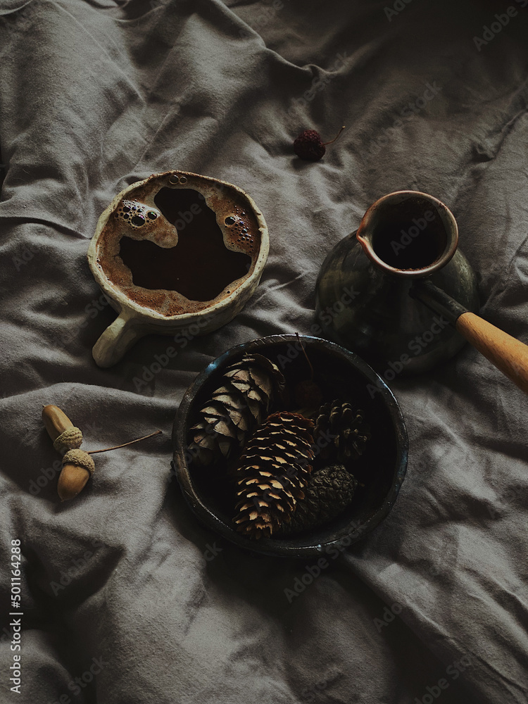 Coffee in rough cup and bump in a bowl and acorn near copper cezve on linens