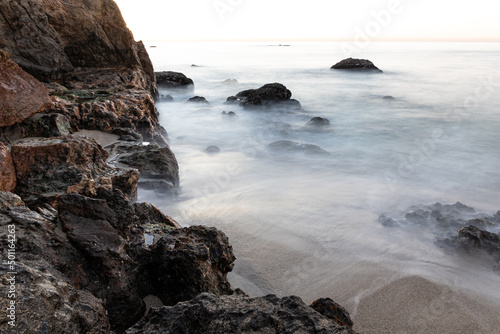 Rocky coastline in the early morning at Malibu, California. Silky waves glide over the sand. 
