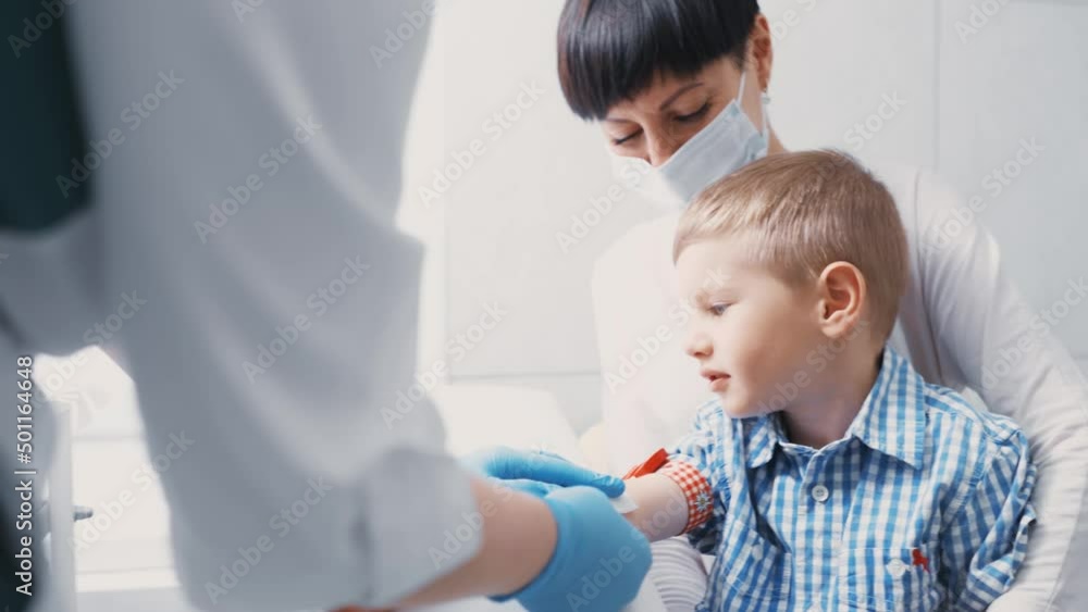 little boy is taking blood from a vein for analysis. The child sits in the arms of his mother in the manipulation room of the clinic. little boy is taking blood from a vein for analysis. The child sits in the arms of his mother in the manipulation room of the clinic.