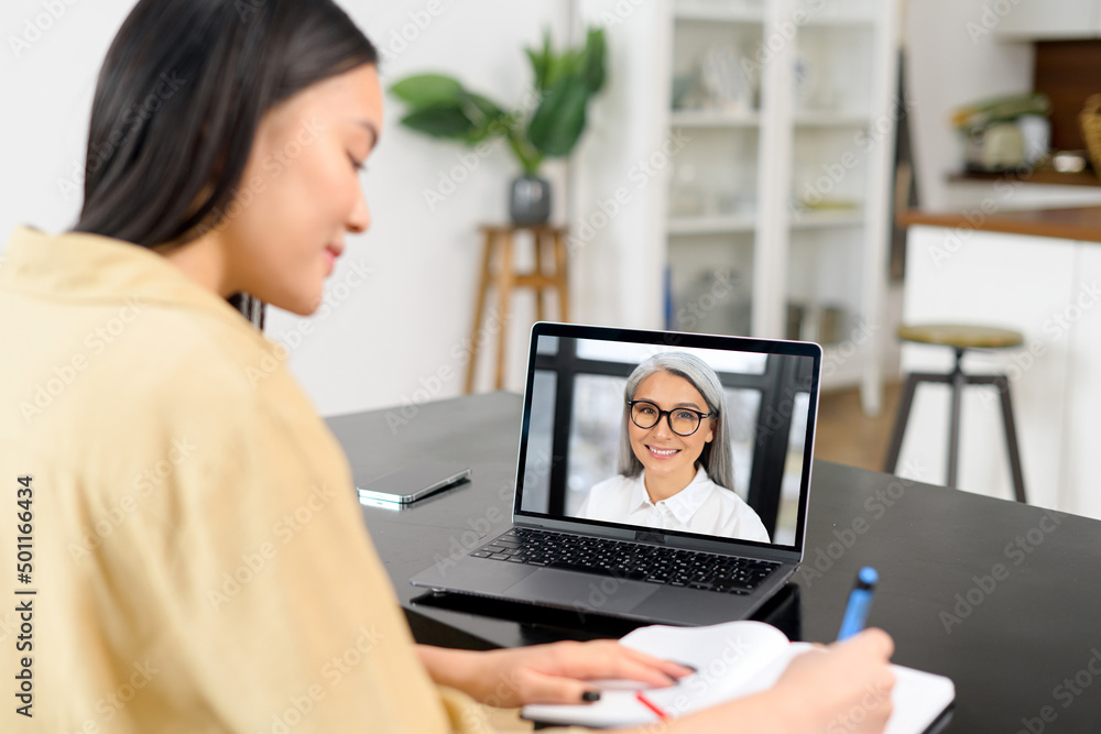 Virtual conference, morning meeting online. Young woman is using app on pc for connection with colleague, employee, she is writing in notebook. Video call with senior woman together Virtual conference, morning meeting online. Young woman is using app on pc for connection with colleague, employee, she is writing in notebook. Video call with senior woman together