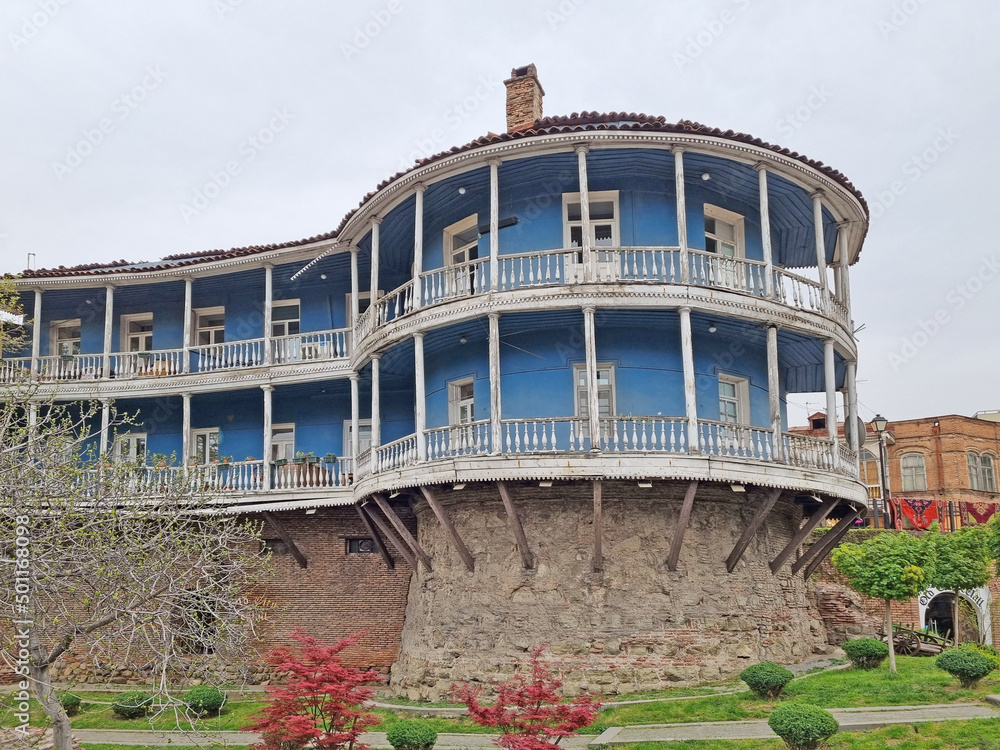 Round-shaped wooden house in the capital of Georgia, Tbilisi, in the Caucasian style with a masonry base and a balcony terrace around  entire perimeter of the building