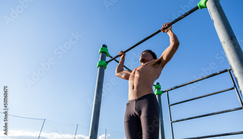Strong guy doing pull up in a calisthenics park. Outdoor training and working out.