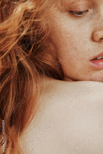 Close-up portrait of young woman with freckles on her face and red hair posing with shirtless back photo