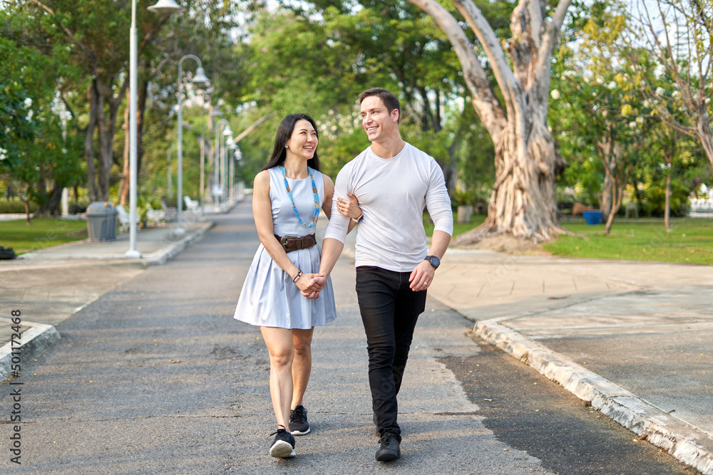 Multiethnic couple walking together on a path in a city park during sunset Multiethnic couple walking together on a path in a city park during sunset