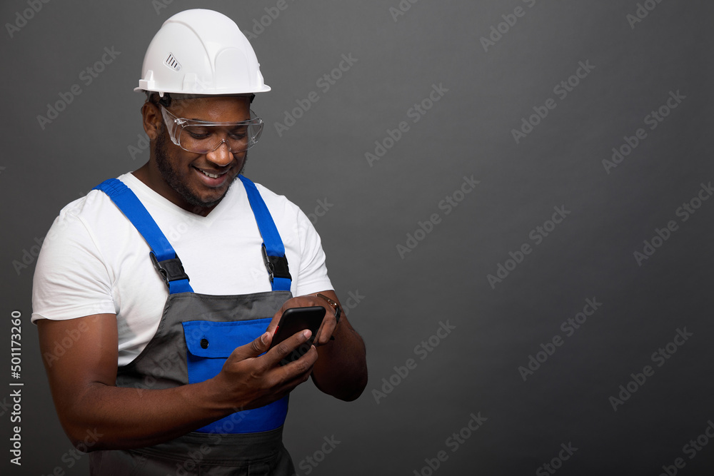 Professional construction worker in protective helmet and glasses corresponds in chat. Black foreman received the good news about the delivery of the material on time in a message on his smartphone Professional construction worker in protective helmet and glasses corresponds in chat. Black foreman received the good news about the delivery of the material on time in a message on his smartphone