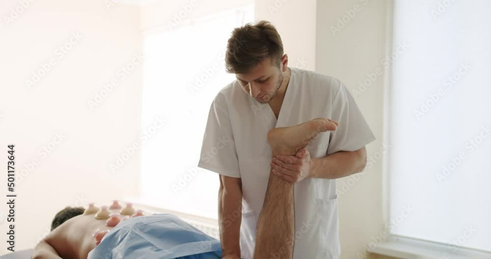 An Adult Man Trains Muscle Strength With a Professional Doctor in a Modern Rehabilitation Clinic. Physiotherapy Program, Rehabilitation After Medical Injuries. Healthcare Concept An Adult Man Trains Muscle Strength With a Professional Doctor in a Modern Rehabilitation Clinic. Physiotherapy Program, Rehabilitation After Medical Injuries. Healthcare Concept