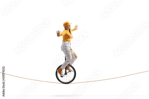 Full length side shot of a young female riding a unicycle on a tightrope