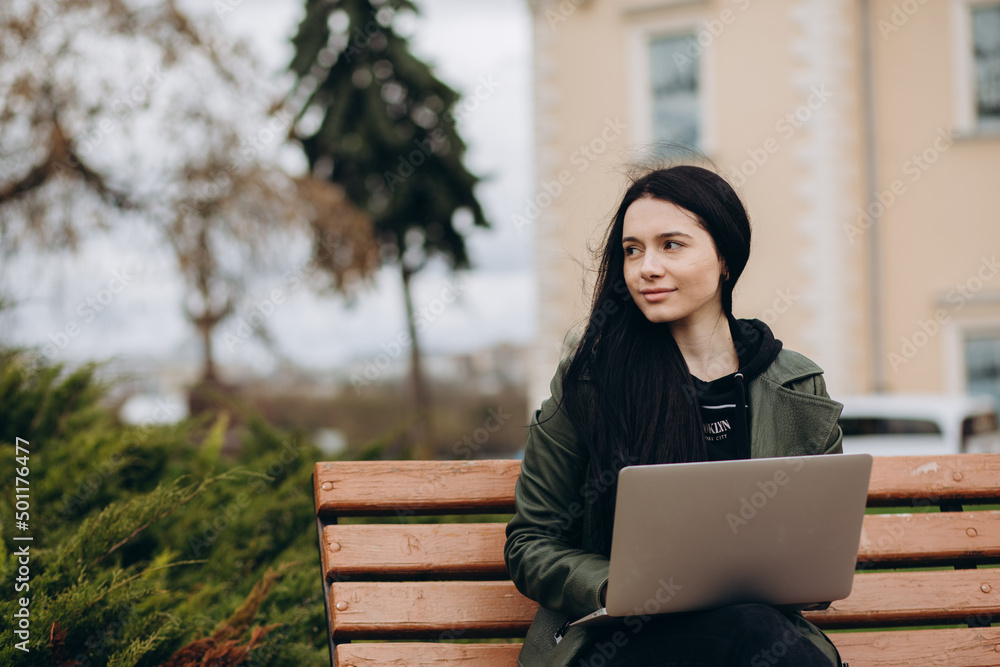 Beautiful young woman sitting in public park chatting over laptop computer Beautiful young woman sitting in public park chatting over laptop computer