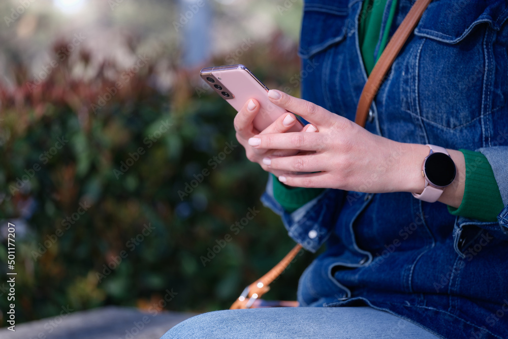 Woman sitting in park and holding mobile phone in her hands closeup