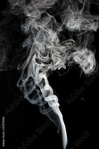 Puffs and curls of white smoke against a black background rising from a burning stick