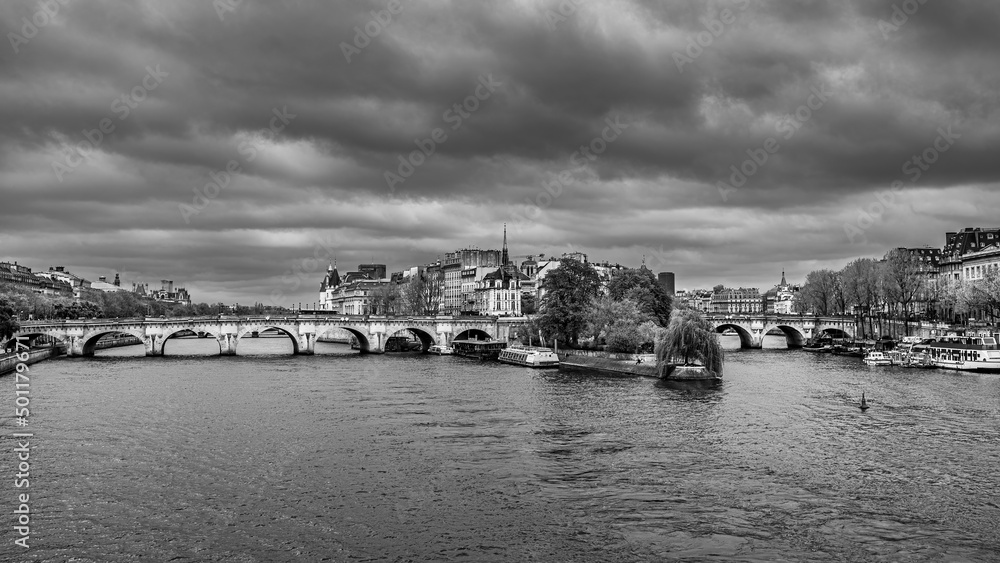 Black and white cityscape of Paris with the Pont Neuf and the Île de la Cité beliw the dense cloudy sky