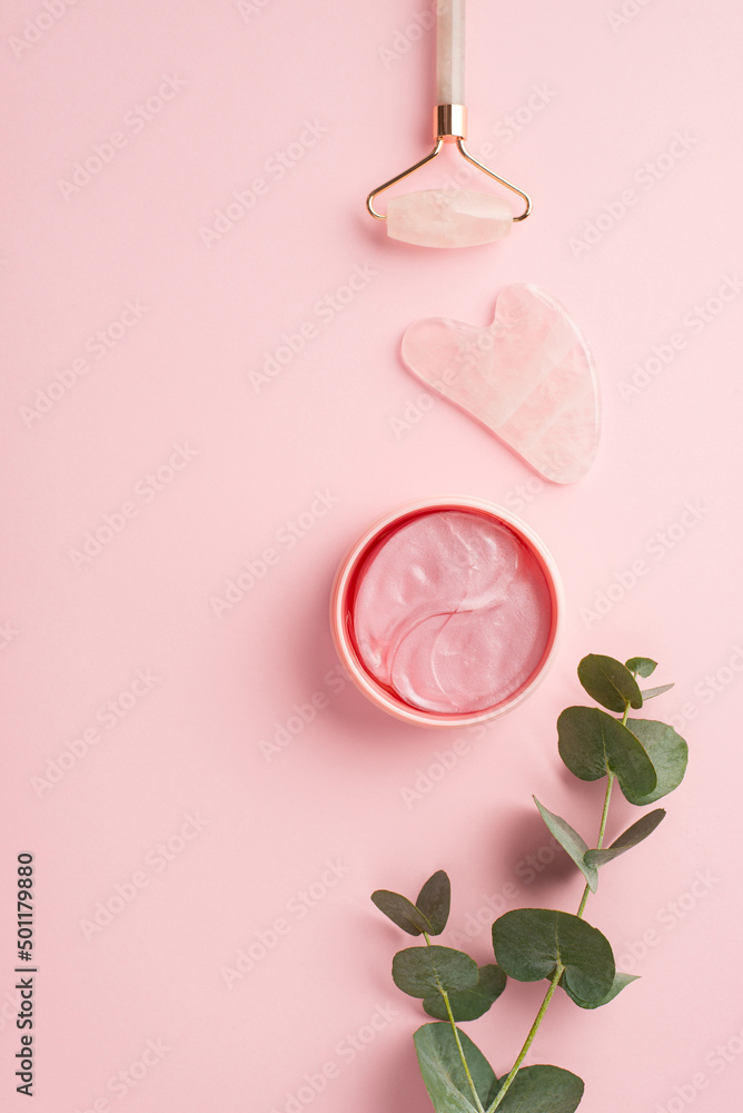 Beauty procedure concept. Top view vertical photo of rose quartz roller gua sha pink eye patches and eucalyptus sprig on isolated pastel pink background Beauty procedure concept. Top view vertical photo of rose quartz roller gua sha pink eye patches and eucalyptus sprig on isolated pastel pink background