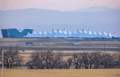 Agricultural landscape with naked spring trees and oil pump in the prairie of Eastern Colorado. The Denver International Airport with the silhouette of the Rocky Mountains is viewable in the distance photo