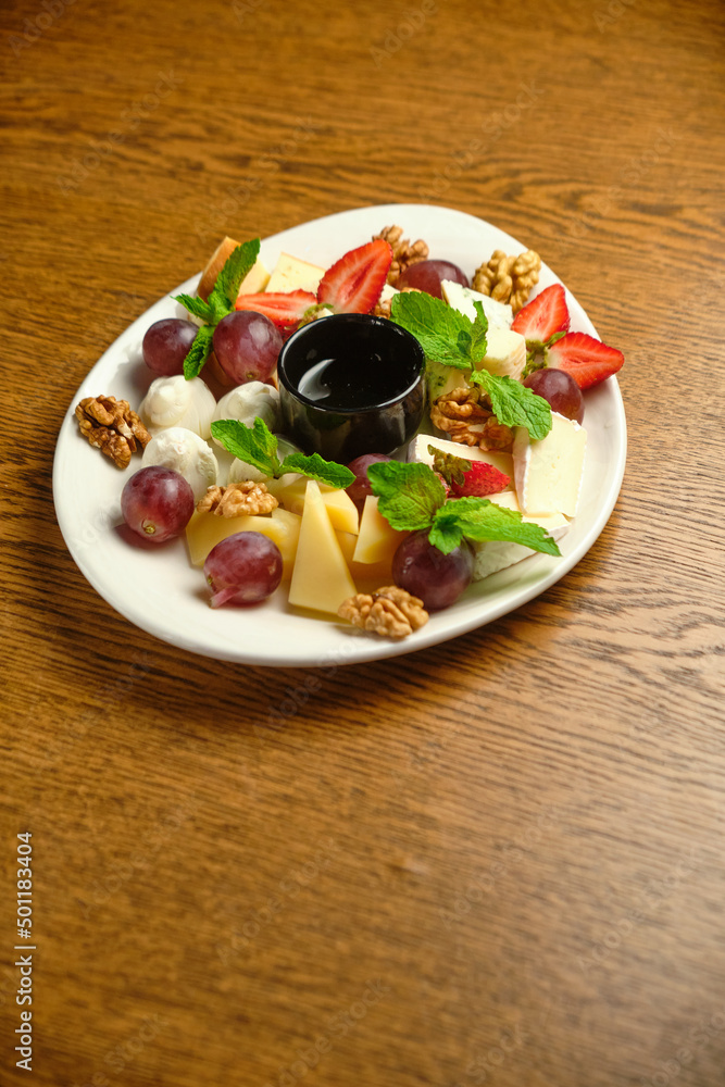 A plate with several varieties of cheese and fruit. Jam sauce in the middle of the plate A plate with several varieties of cheese and fruit. Jam sauce in the middle of the plate