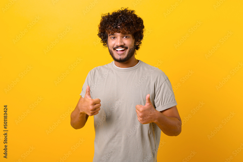 Like, excellent job. Pleased Indian man smiling to camera and gesturing thumbs up, approval hand sign, satisfied with result. Indoor studio shot isolated on yellow background Like, excellent job. Pleased Indian man smiling to camera and gesturing thumbs up, approval hand sign, satisfied with result. Indoor studio shot isolated on yellow background