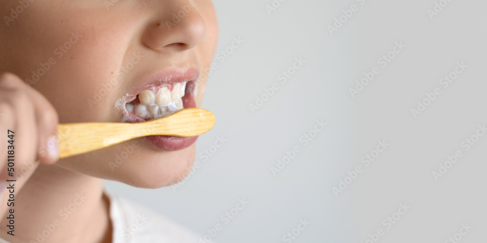 Close up portrait child brush teeth with eco wooden toothbrush, isolated on light background. Dental hygiene, morning routine, healthy lifestyle, medical care. Side view Copy space Close up portrait child brush teeth with eco wooden toothbrush, isolated on light background. Dental hygiene, morning routine, healthy lifestyle, medical care. Side view Copy space